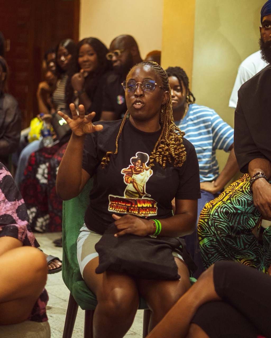 A woman in glasses speaking from her seat at a past hangout, the room listening